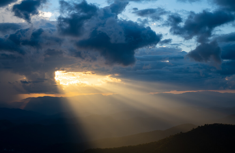 he bright rays of the sun are shining from saturated clouds to mountain. CREDIT: PhilipYb Studio/Shutterstock.com.