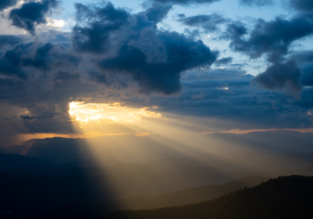 明亮的阳光从饱和的云层中洒向山峰。图片来源：PhilipYb Studio/Shutterstock.com。