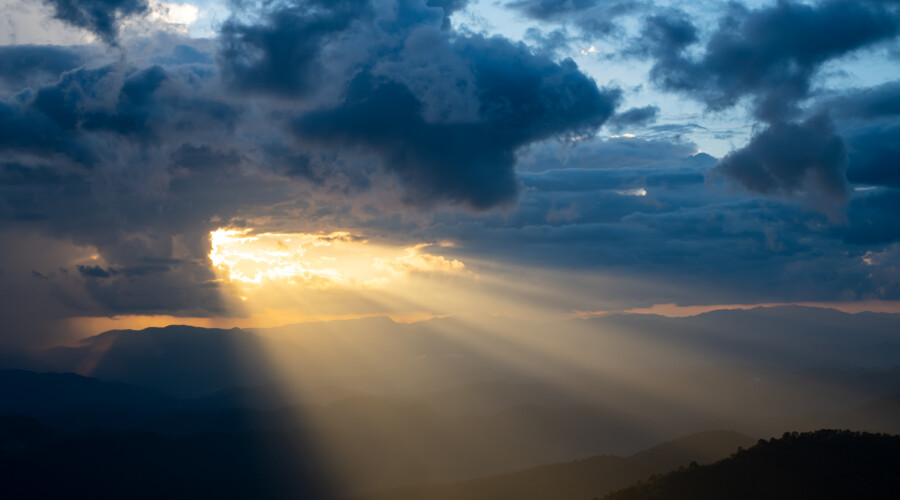 he bright rays of the sun are shining from saturated clouds to mountain. CREDIT: PhilipYb Studio/Shutterstock.com.